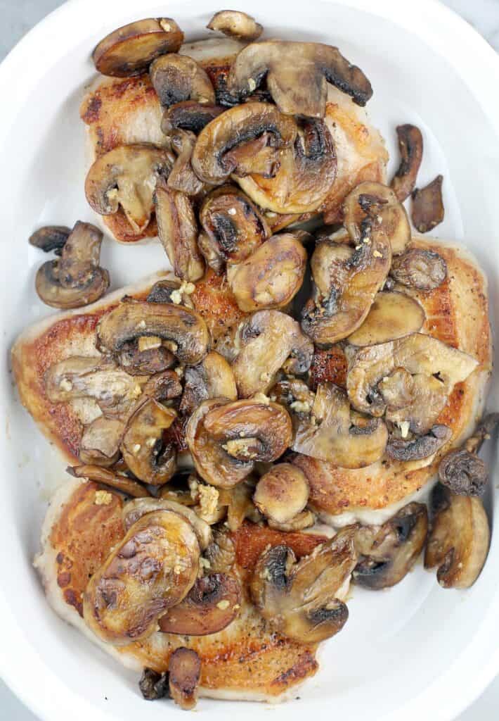 top view of browned mushrooms on the seared chops in a white bake dish