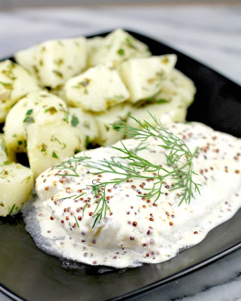 finished baked fish on a black dish on a marble surface. Herbed potatoes are in the background