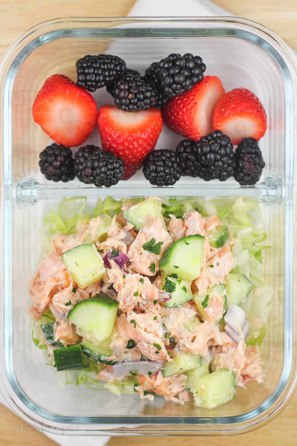 divided glass container with salmon salad in one section, berries in the other