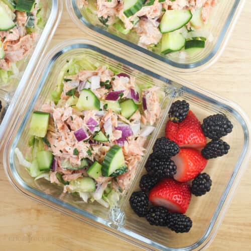 divided glass container with salmon salad in one section, berries in the other