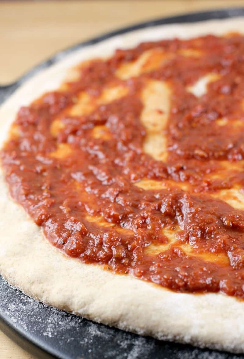 uncooked pizza dough with sauce spread on, on a black pizza stone