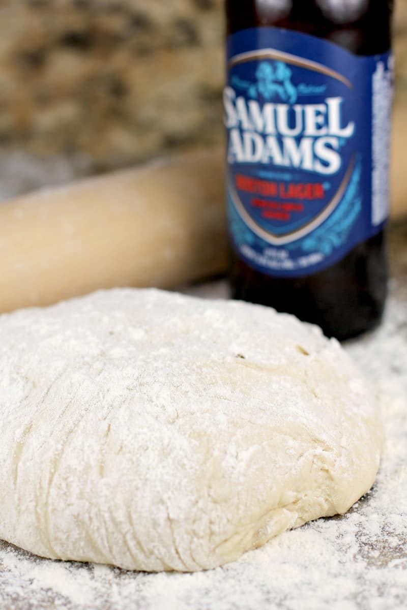 homemade pizza dough on a granite surface with a rolling pin and sam adams beer bottle
