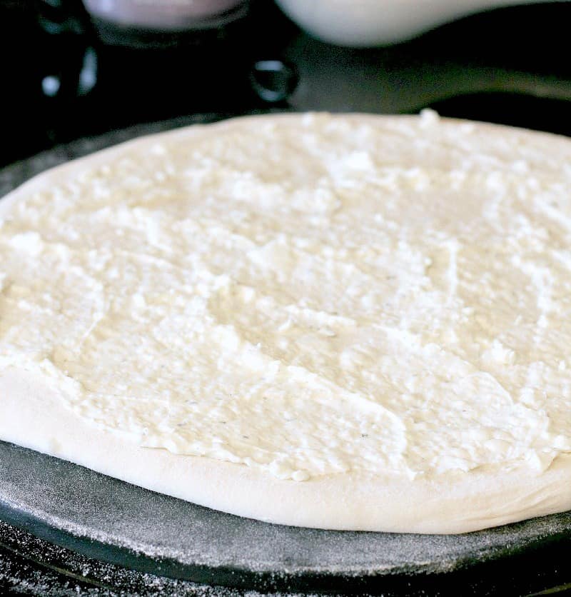 pizza dough rolled out on a stone, topped with the cream cheese sauce, the basis for the jalapeno cheese dip of this pizza