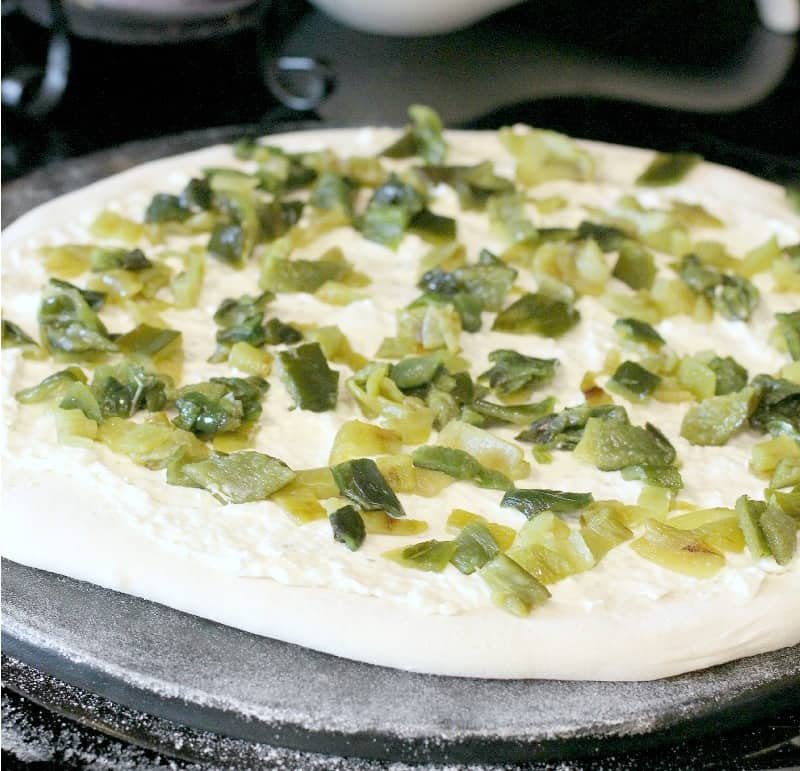 pizza dough rolled out on a stone, topped with sauce and peppers