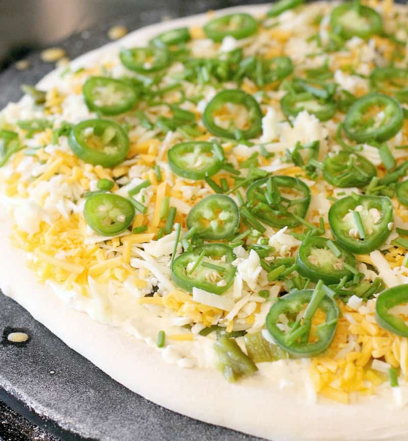 pizza dough rolled out on a stone, topped with the toppings ready for the oven