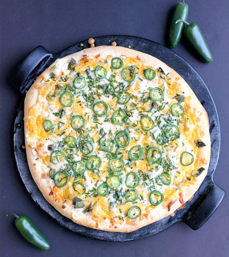 top down view of the finished pizza on the pizza stone with a black background. a couple jalapenos are scattered around