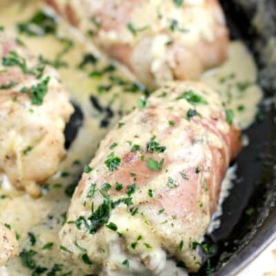 chicken thighs in a cast iron skillet, wrapped in prosciutto, cheese sauce spooned over