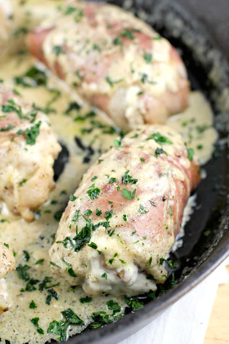 chicken thighs in a cast iron skillet, wrapped in prosciutto, cheese sauce spooned over