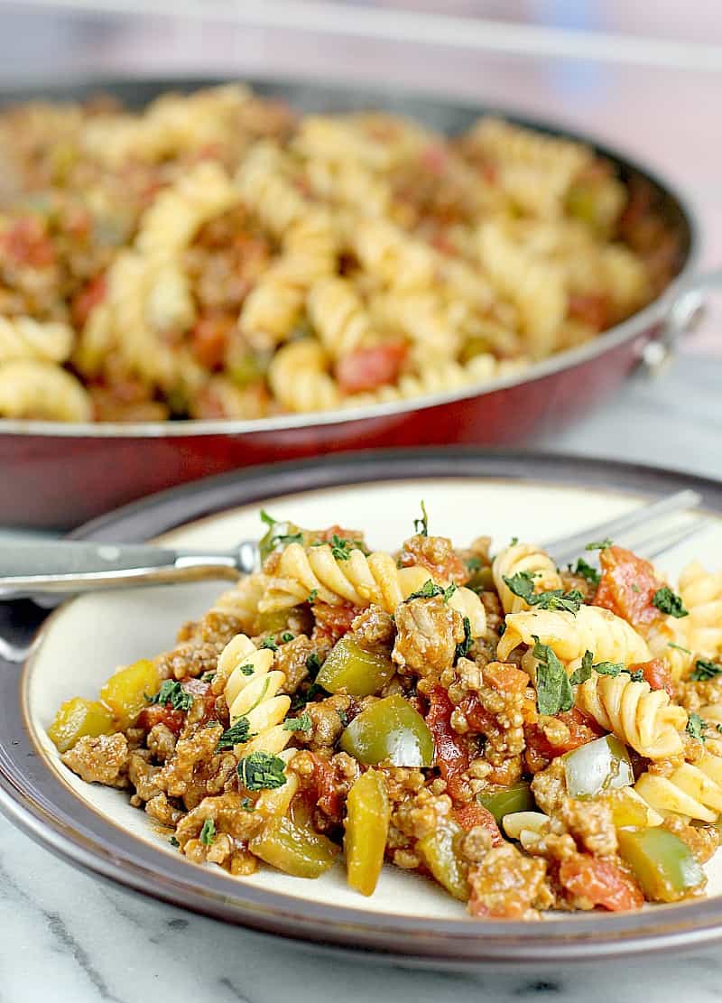 finished cheap dinner idea for sloppy joe pasta plated on a white and brown plate, placed on white marble board. Fork on the plate. Rest of the meal is in a skillet in the background