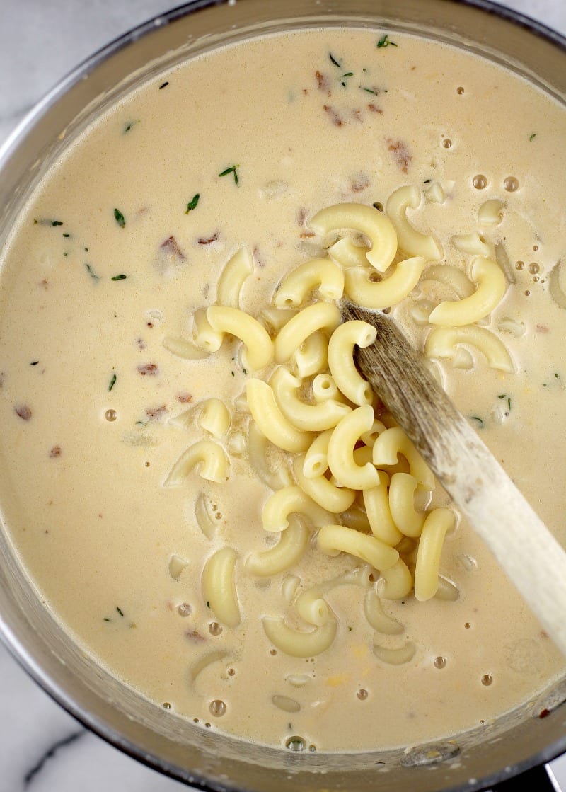 macaroni being added to the cheese sauce, top down view in a saucepan