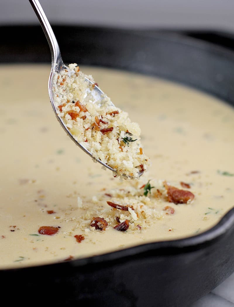 cast iron skillet, side view showing the topping being sprinkled on with a spoon to the mac and cheese