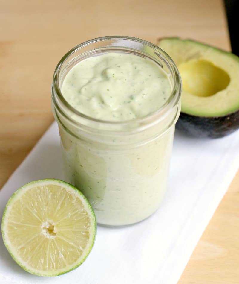 mason jar filled with the dressing next to a lime and avocado