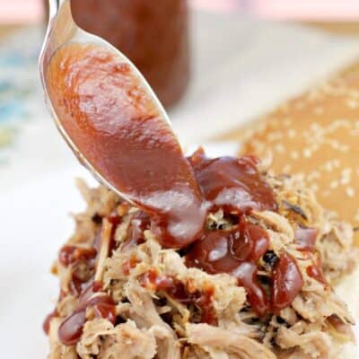 spoon putting chipotle bbq sauce on pulled pork on a bun