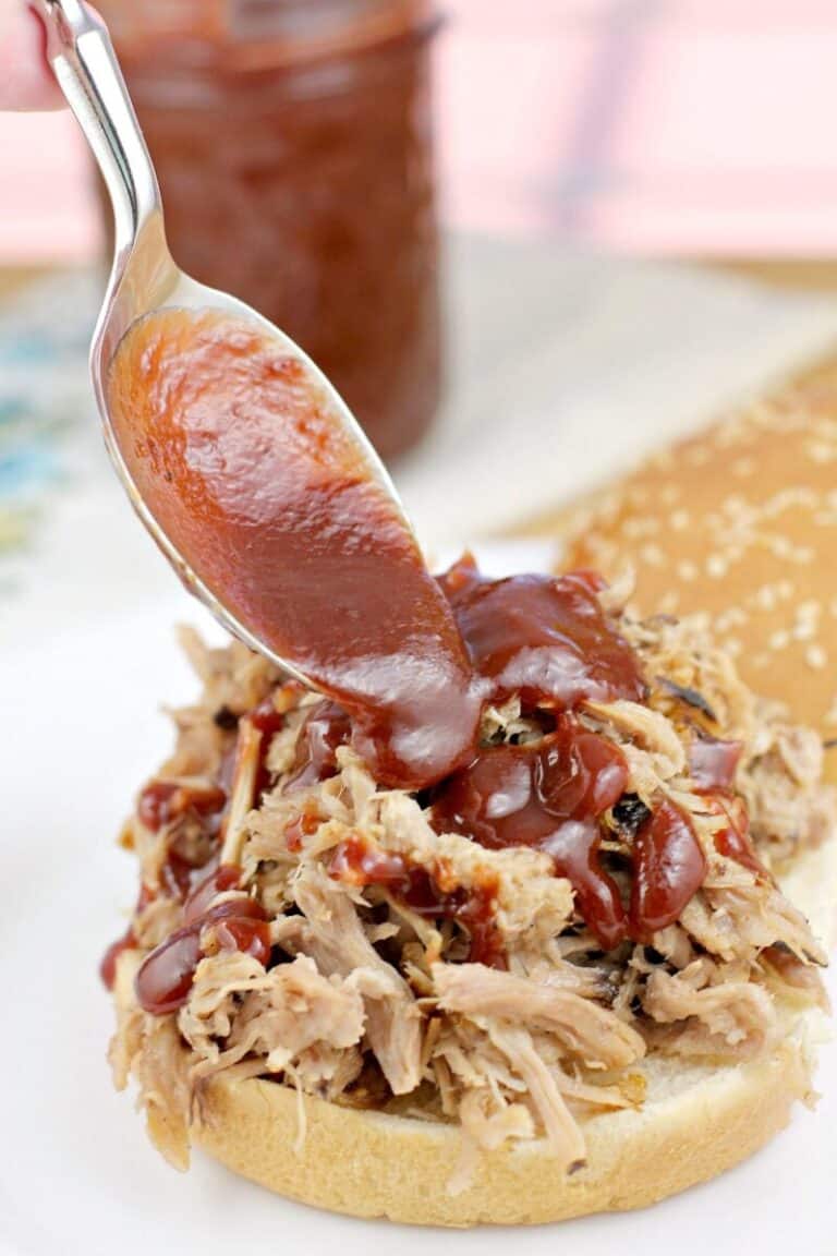 spoon putting chipotle bbq sauce on pulled pork on a bun