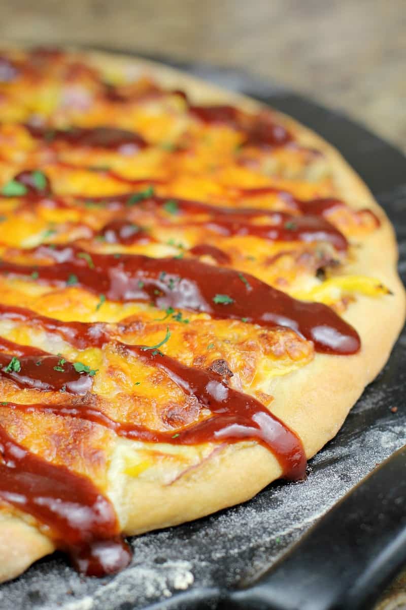 cooked pizza on pizza stone drizzled with sauce