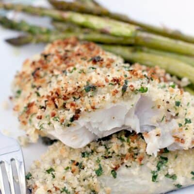 serving of baked haddock with panko on white plate with asparagus and a fork