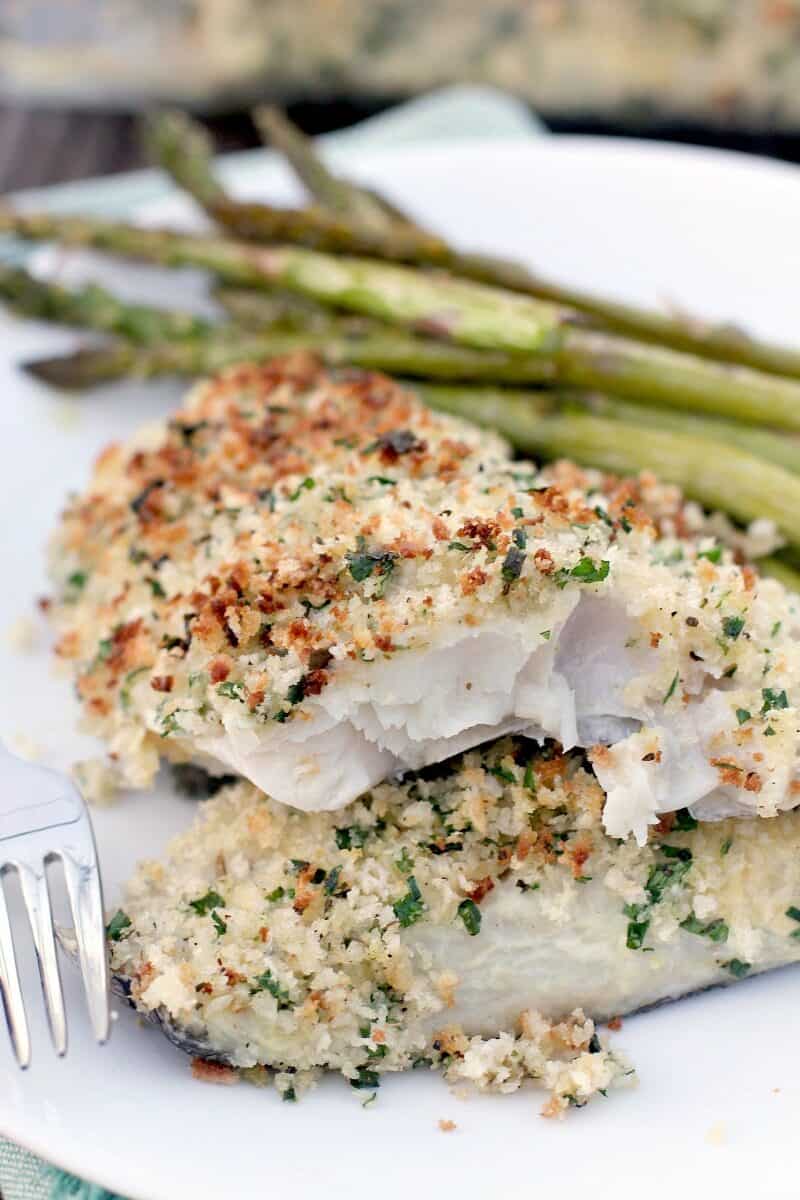 serving of baked haddock with panko on white plate with asparagus and a fork