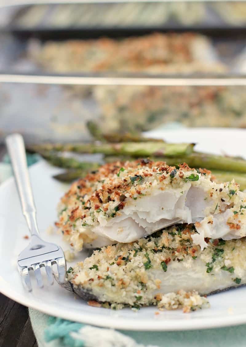 cooked fish on white plate with fork and asparagus