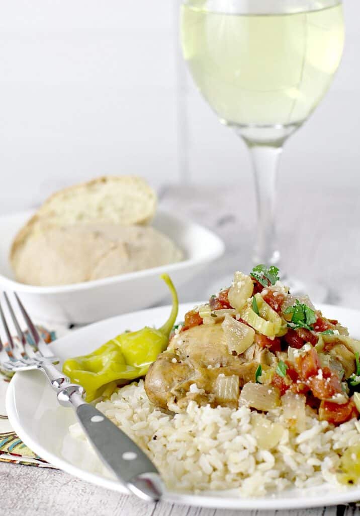 view showing cooked slow cooker italian pepperoncini chicken served over rice. Bread and glass of white wine are in the background.