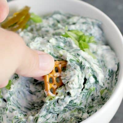 hand scooping a pretzel into spinach dip