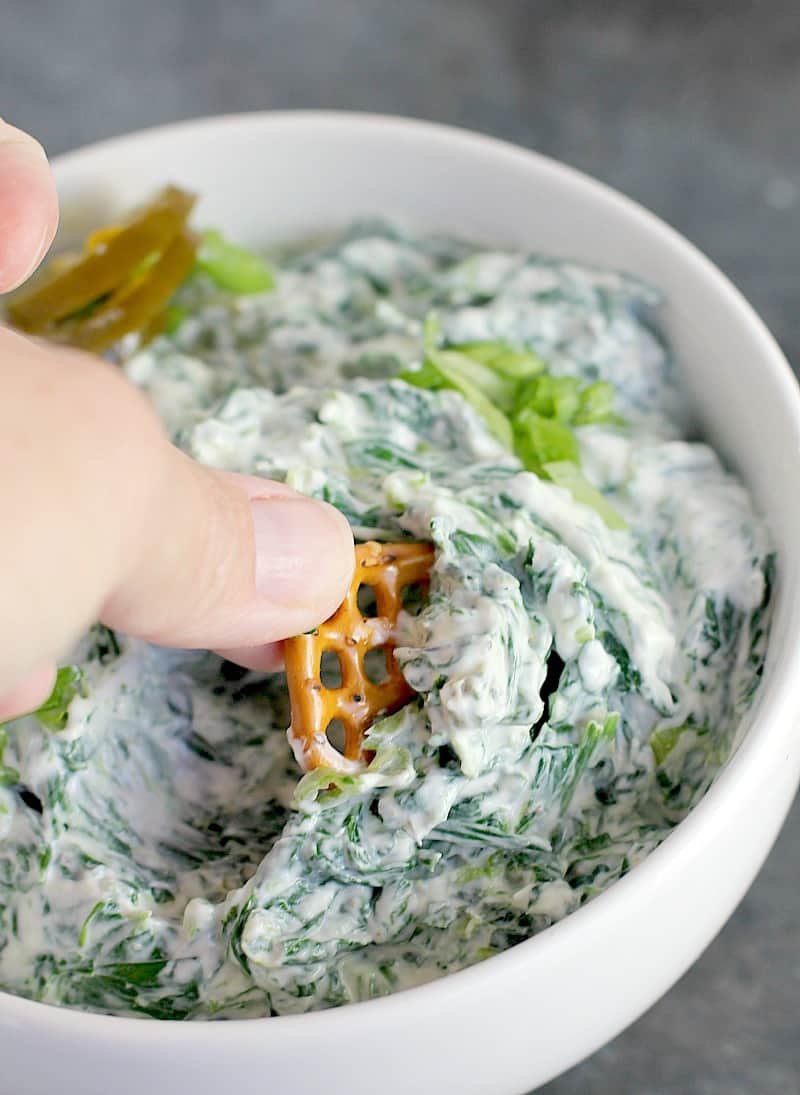 hand scooping a pretzel into spinach jalapeno dip