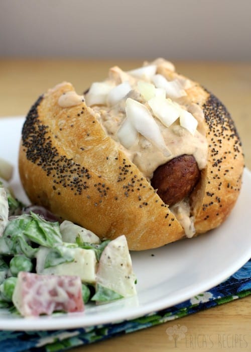 angled view of the finished Grilled Beer Kielbasa with Sausage and Stout Queso, topped with onions, on a white place with a bit of salad on the side