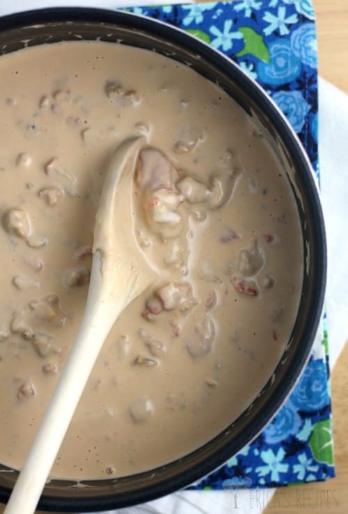 The finished sausage and Guiness extra stout beer cheese sauce in a saucepan with a wooden spoon; blue floral napkin in the background