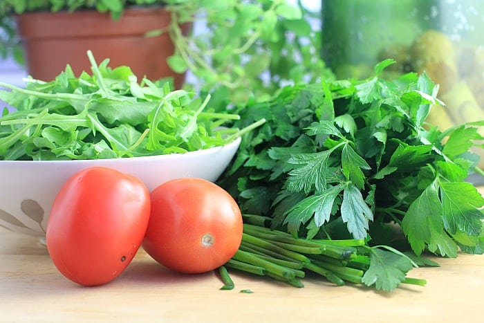 tomatoes, arugula, and parsley on a cutting board