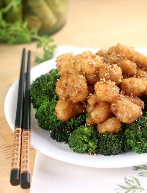 crispy shrimp over broccoli on a white plate with black chopsticks