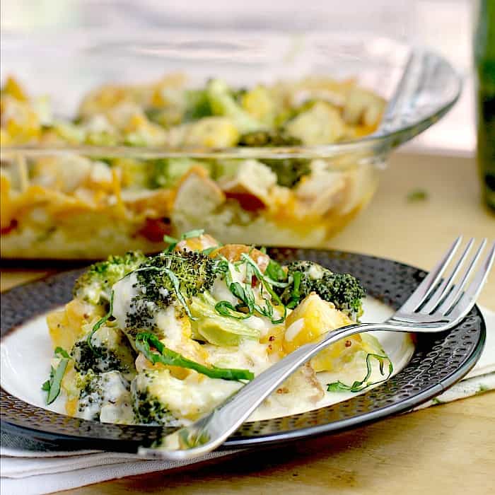 broccoli casserole with cheese on rimmed with with fork. dish is on napkin, on wood surface