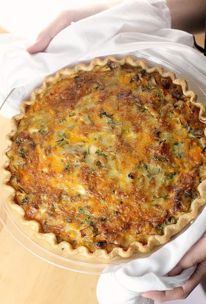 hands holding cooked quiche in white dish towel