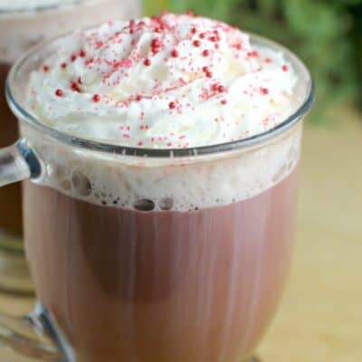 red velvet latte in a glass mug on a wood board; second cup and green leaves of a plant in the background