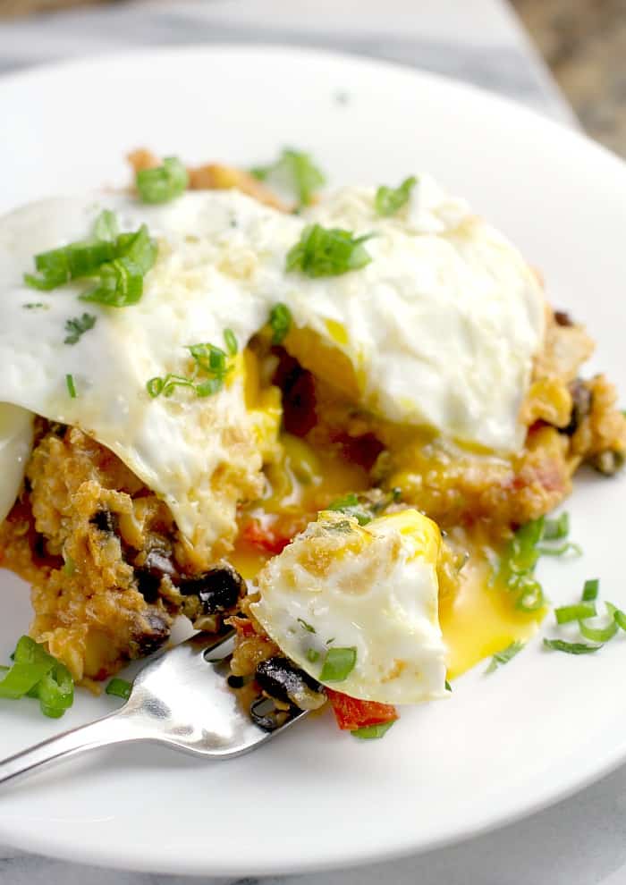 over easy egg on serving of tamale casserole on white plate with fork