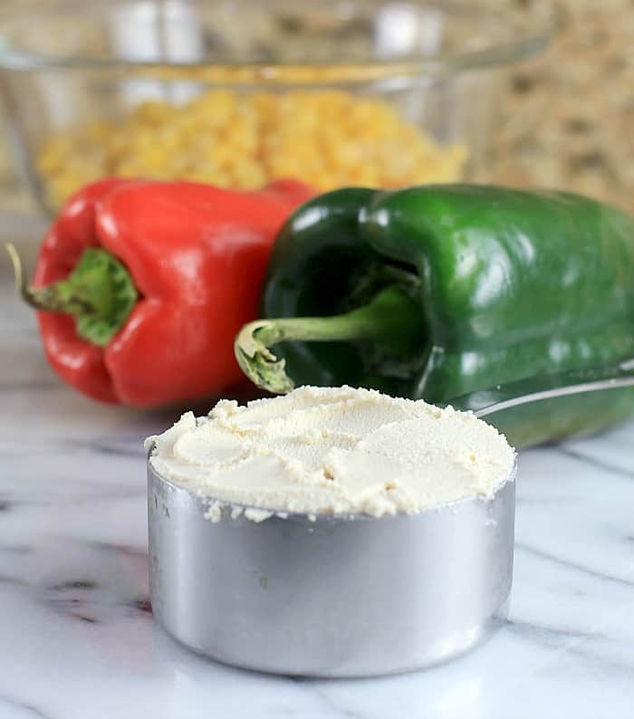 metal measuring cup with cashew ricotta; peppers in the background