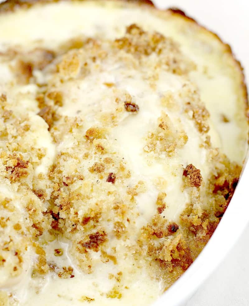 baked chicken in a white casserole dish topped with browned topping and surrounded with bubbly sauce