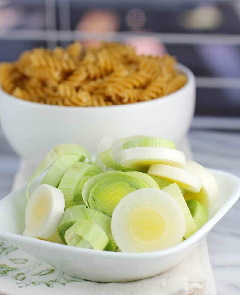 sliced leeks in a small white bowl; uncooked pasta in the background