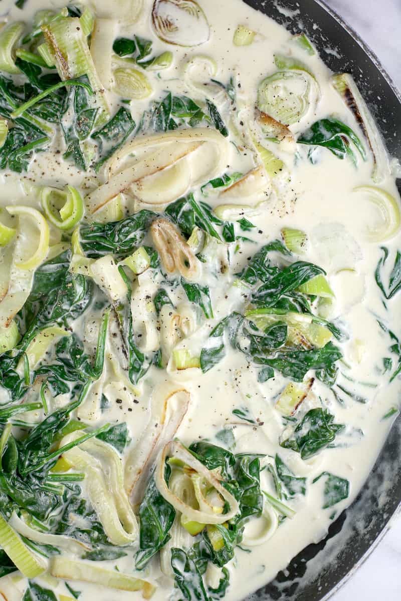 completed cream sauce in a skillet with cooked leeks and spinach