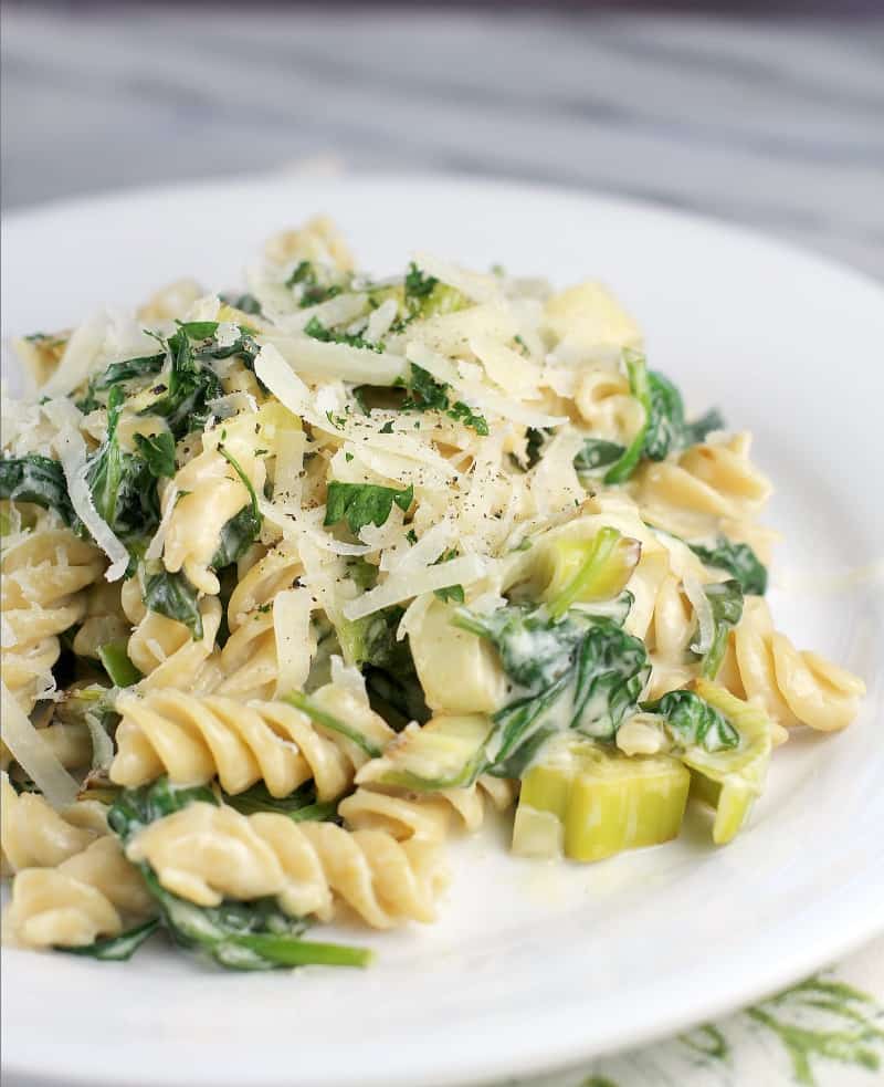 rotini pasta with leeks and spinach on a white plate, topped with cheese