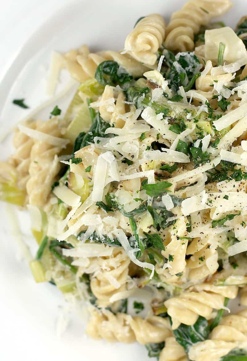 top view rotini pasta with leeks and spinach on a white plate, topped with cheese