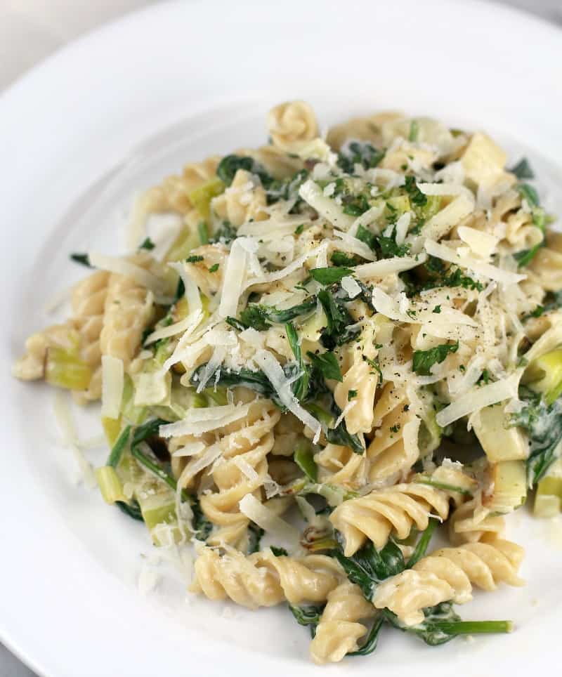 rotini pasta with leeks and spinach on a white plate, topped with cheese
