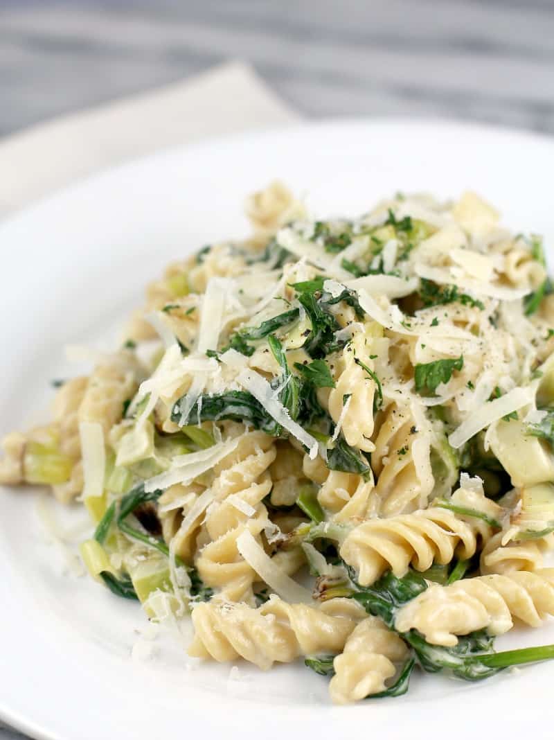 rotini pasta with leeks and spinach on a white plate, topped with cheese