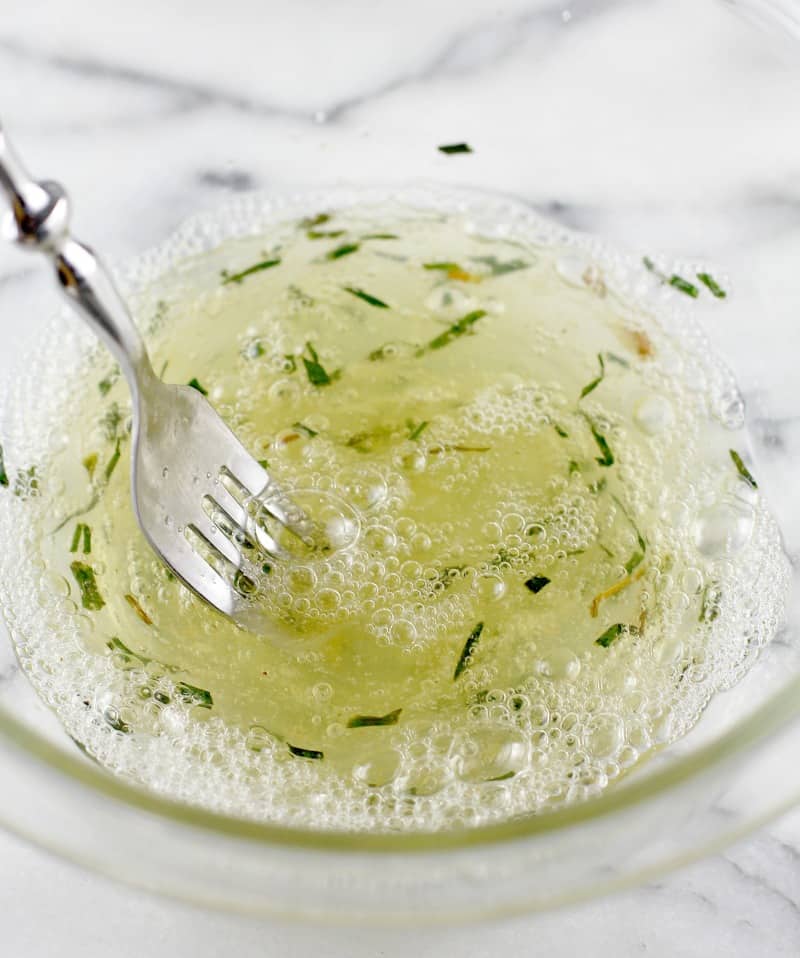 glass bowl with egg whites, herbs, and seasoning being stirred with a fork