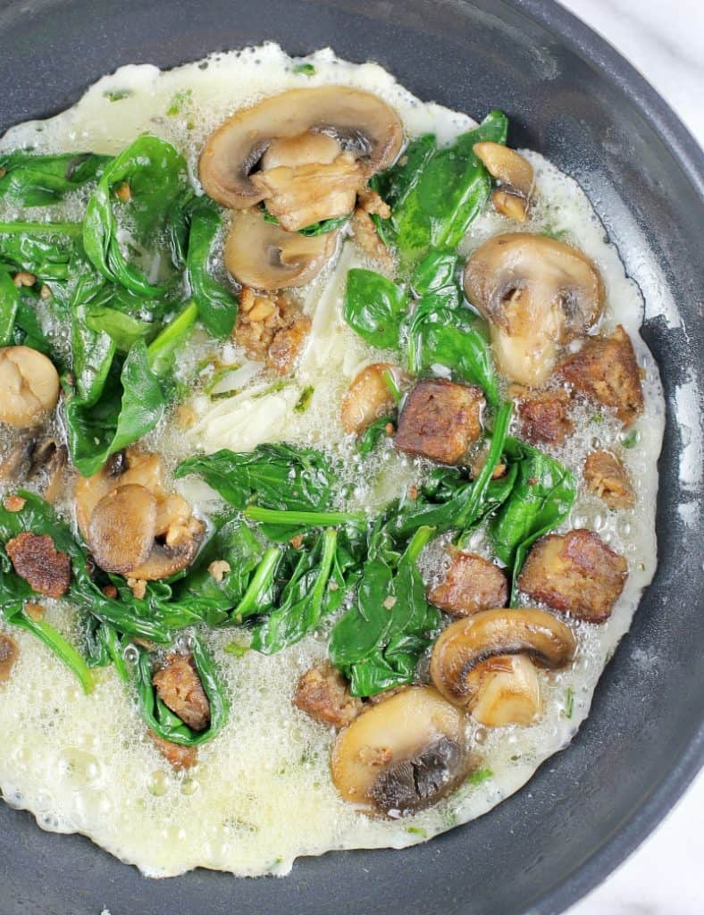 skillet with the egg whites cooking, topped with spinach mushrooms and sausage