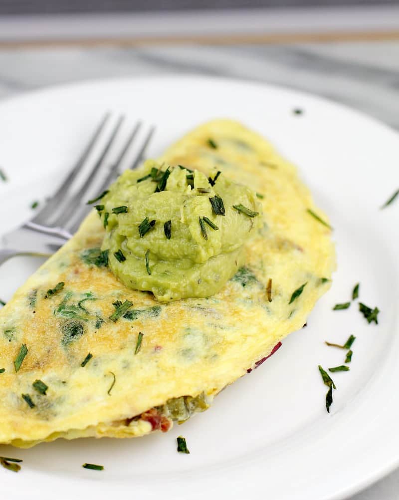 Omelet on white plate, topped with dollop of guacamole, snipped chives sprinkled over. Fork in the background.