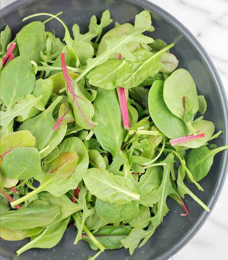 Top down view of fresh mixed salad greens including Swiss chard, baby spinach, and arugula in a skillet.