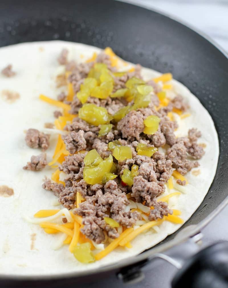 open quesadilla cooking in the pan showing cheese, meat, and pickle