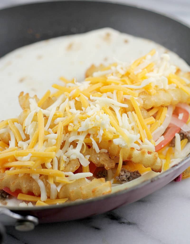 all the toppings layered in an open tortilla cooking in the pan