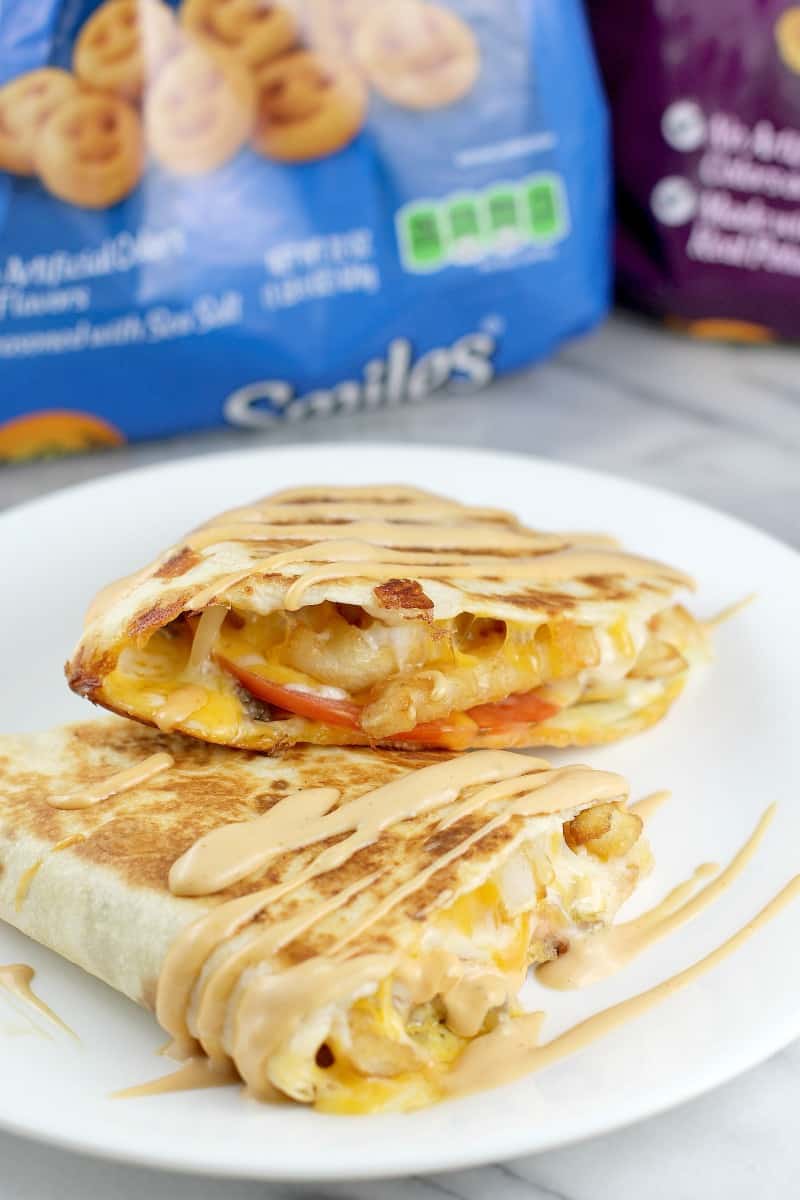 angle view of finished quesadilla, cut in half to show filling; bag of McCain Smiles in the background