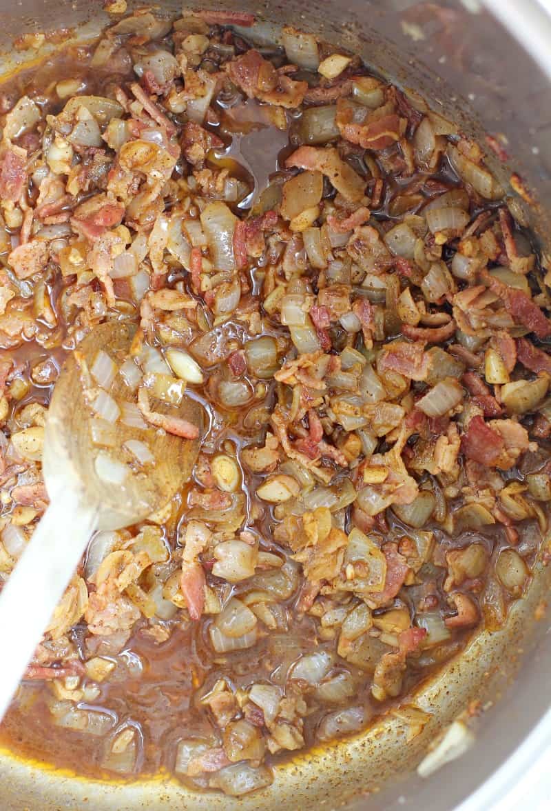 bacon, onion, garlic, and jalapeno cooking in a pot stirred with a wooden spoon