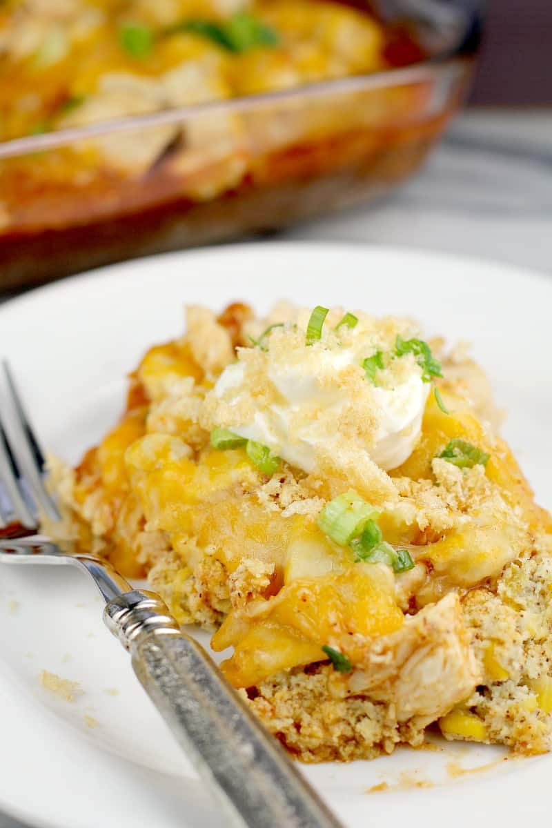 Top down view of finished casserole plated on a white plate with a silver fork, topped with sour cream and pork rind crumbs